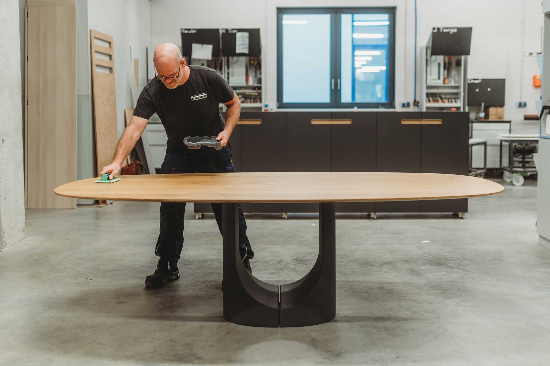 Handwerker arbeitet mit präzisem Werkzeug an einer Holzplatte in der Produktionshalle von Kampfmann Inneneinrichtungen﻿